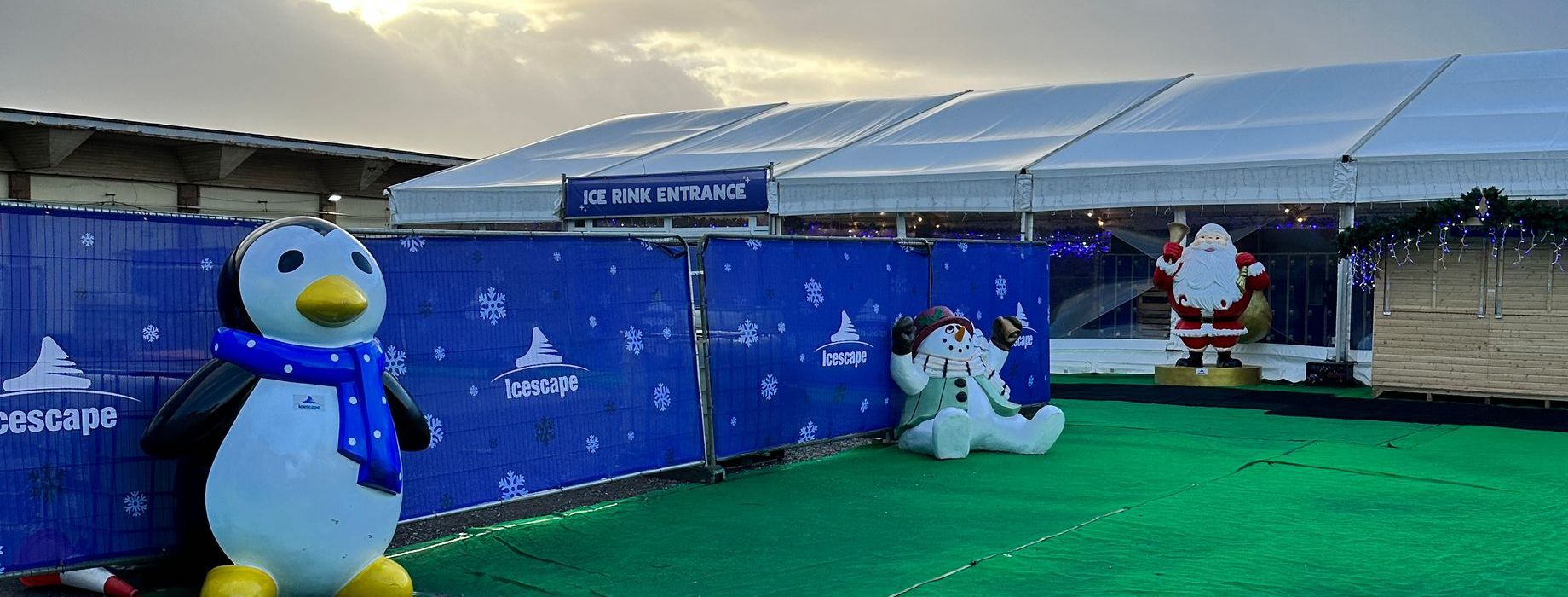A penguin and a santa claus statue are sitting in front of a tent.