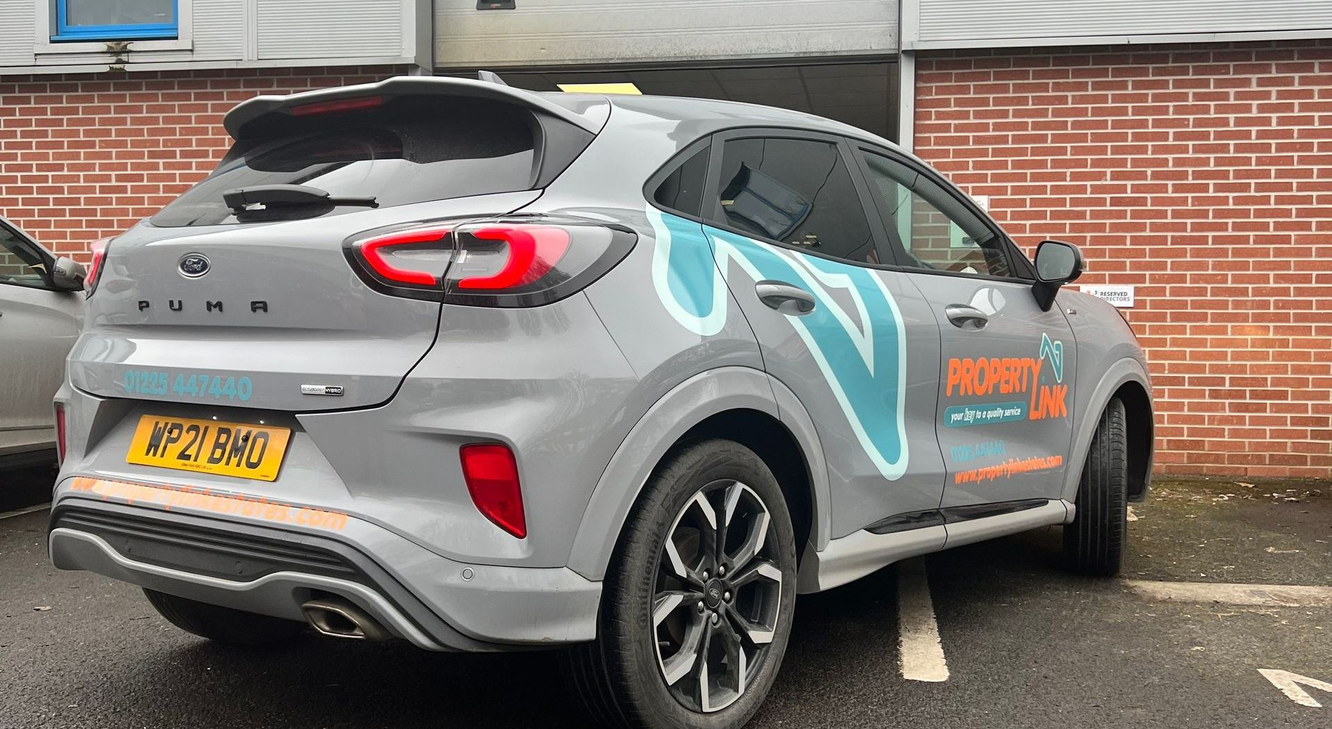 A ford puma is parked in a parking lot in front of a brick building.