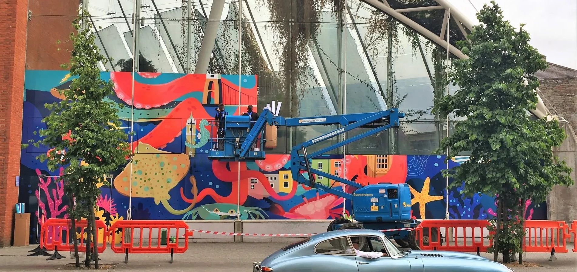 A car is parked in front of a building with a mural on it.