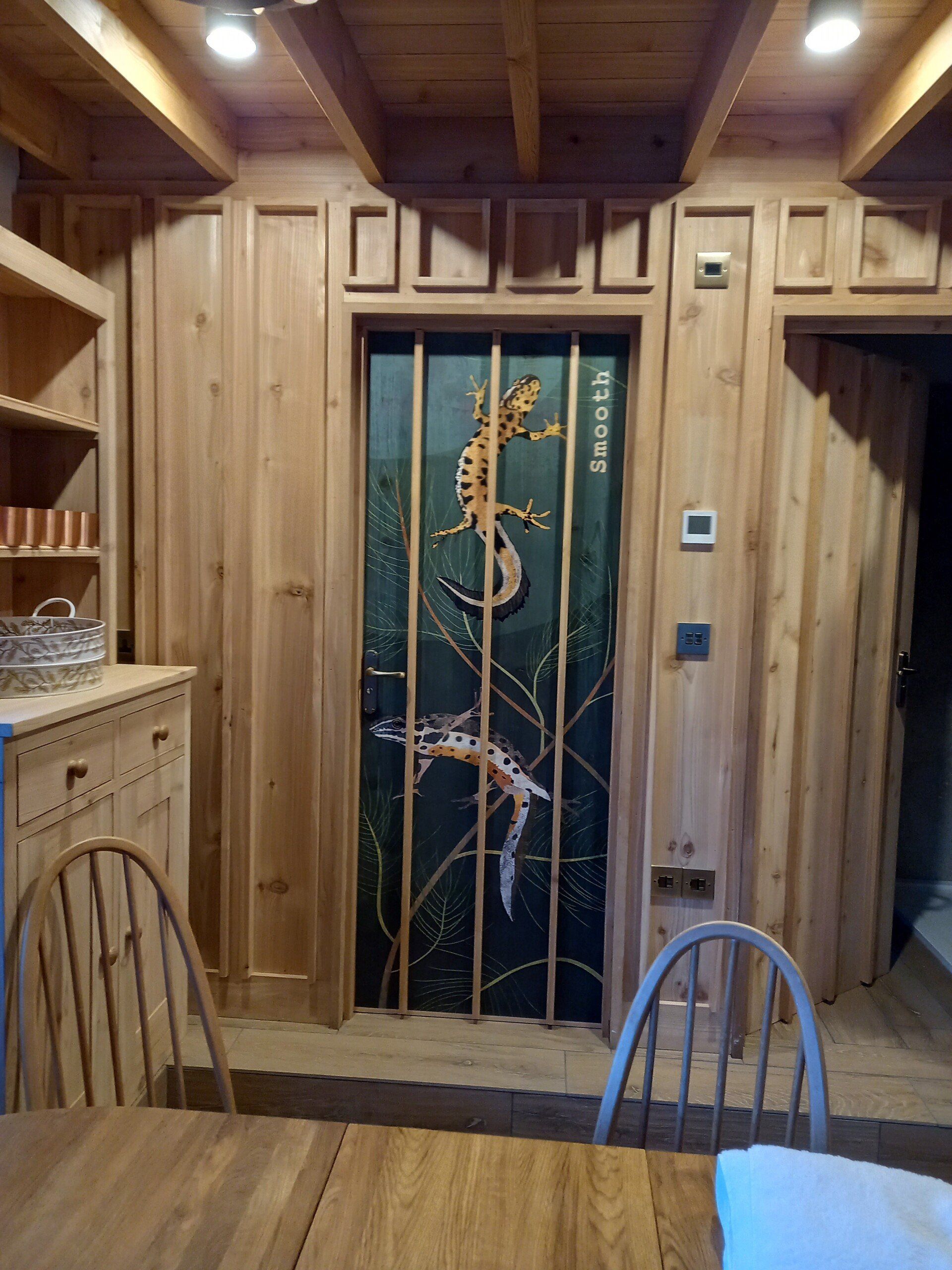 A wooden room with a table and chairs and a door with a lizard on it.