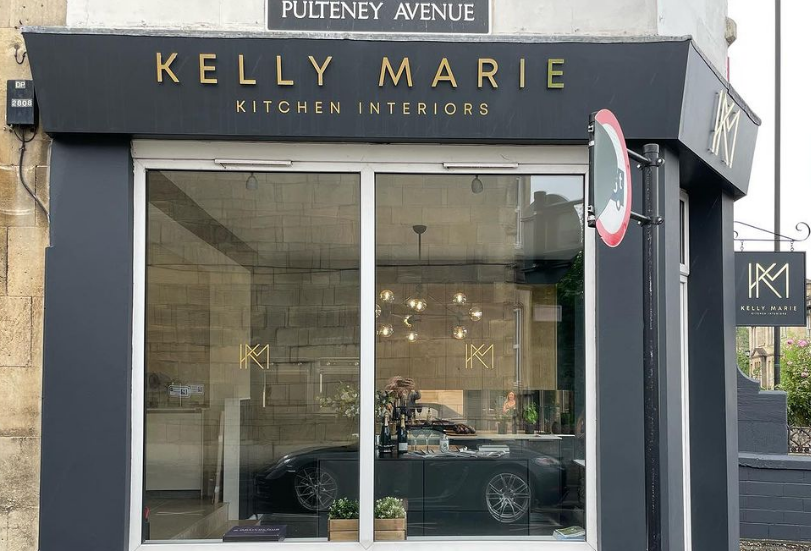 A kelly marie kitchen interiors store front with a car parked in front of it.