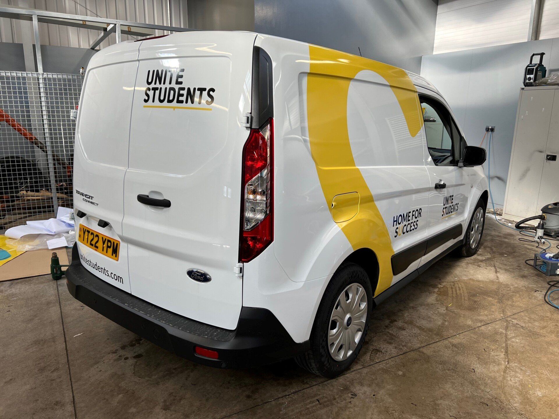 A white van with a yellow stripe on the side is parked in a garage.