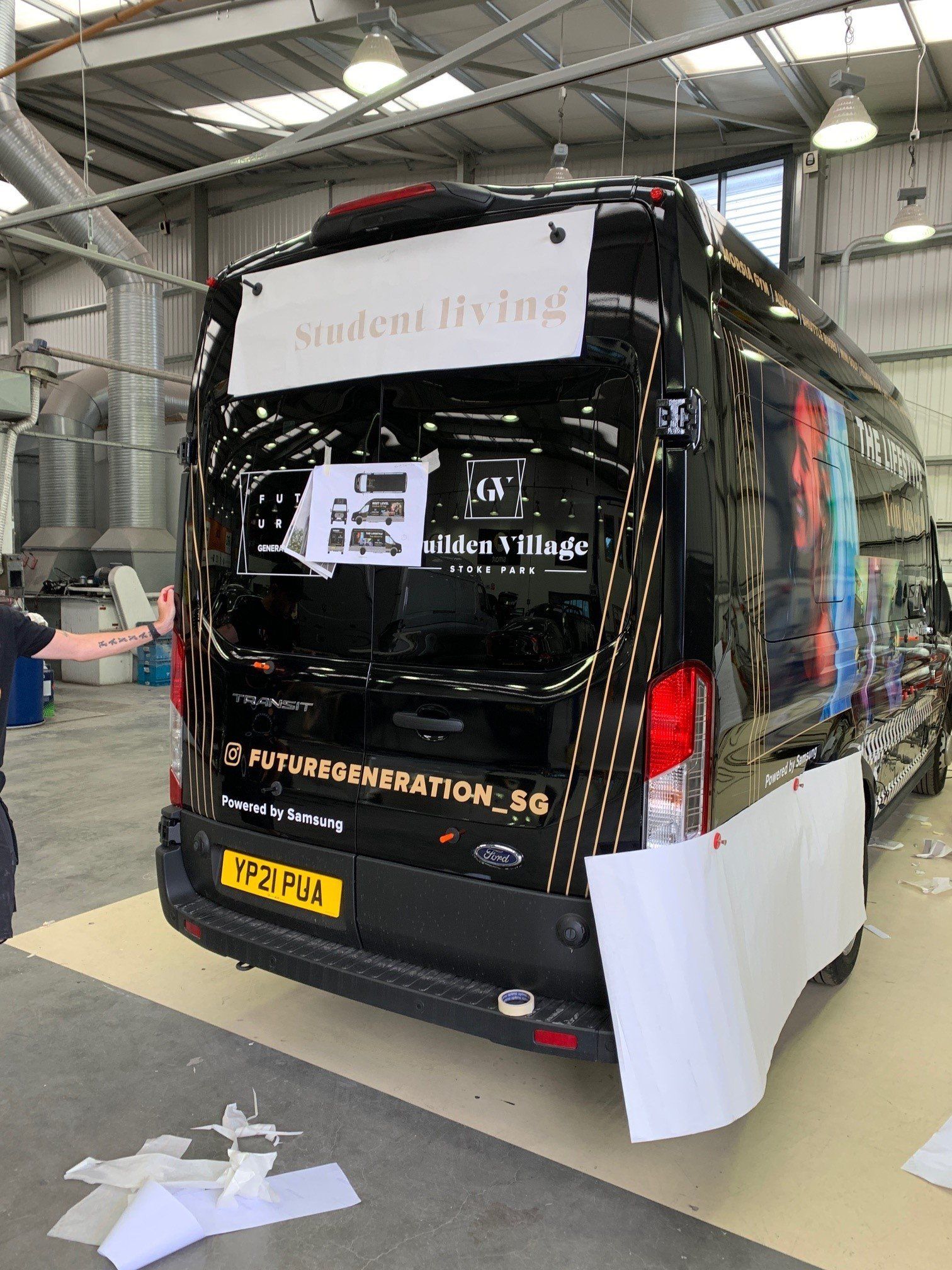 A black van is being wrapped in a warehouse.