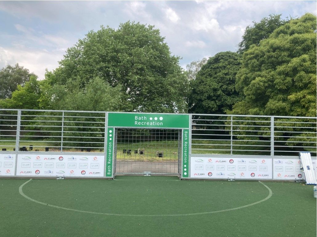 A soccer field with a green gate and trees in the background.