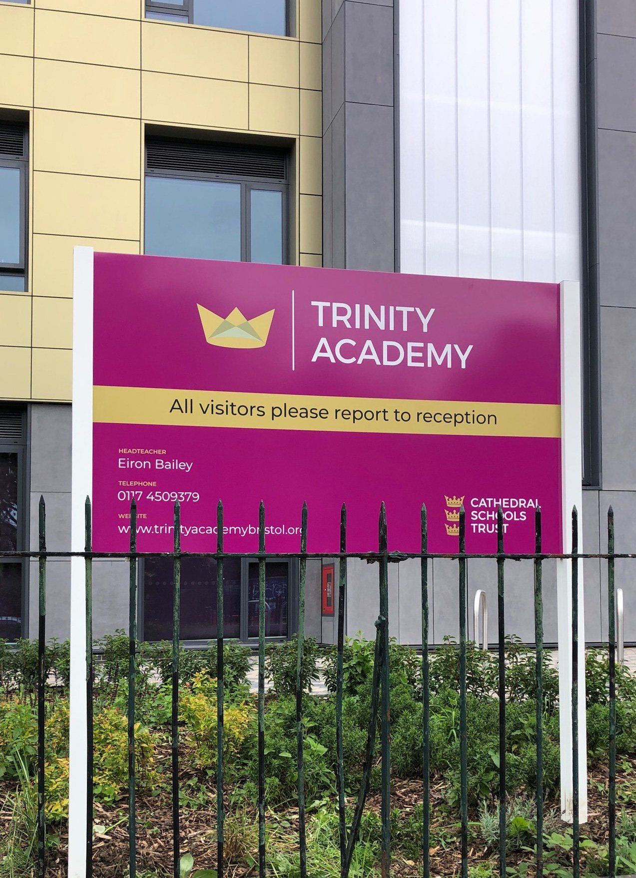 A sign for trinity academy is behind a fence
