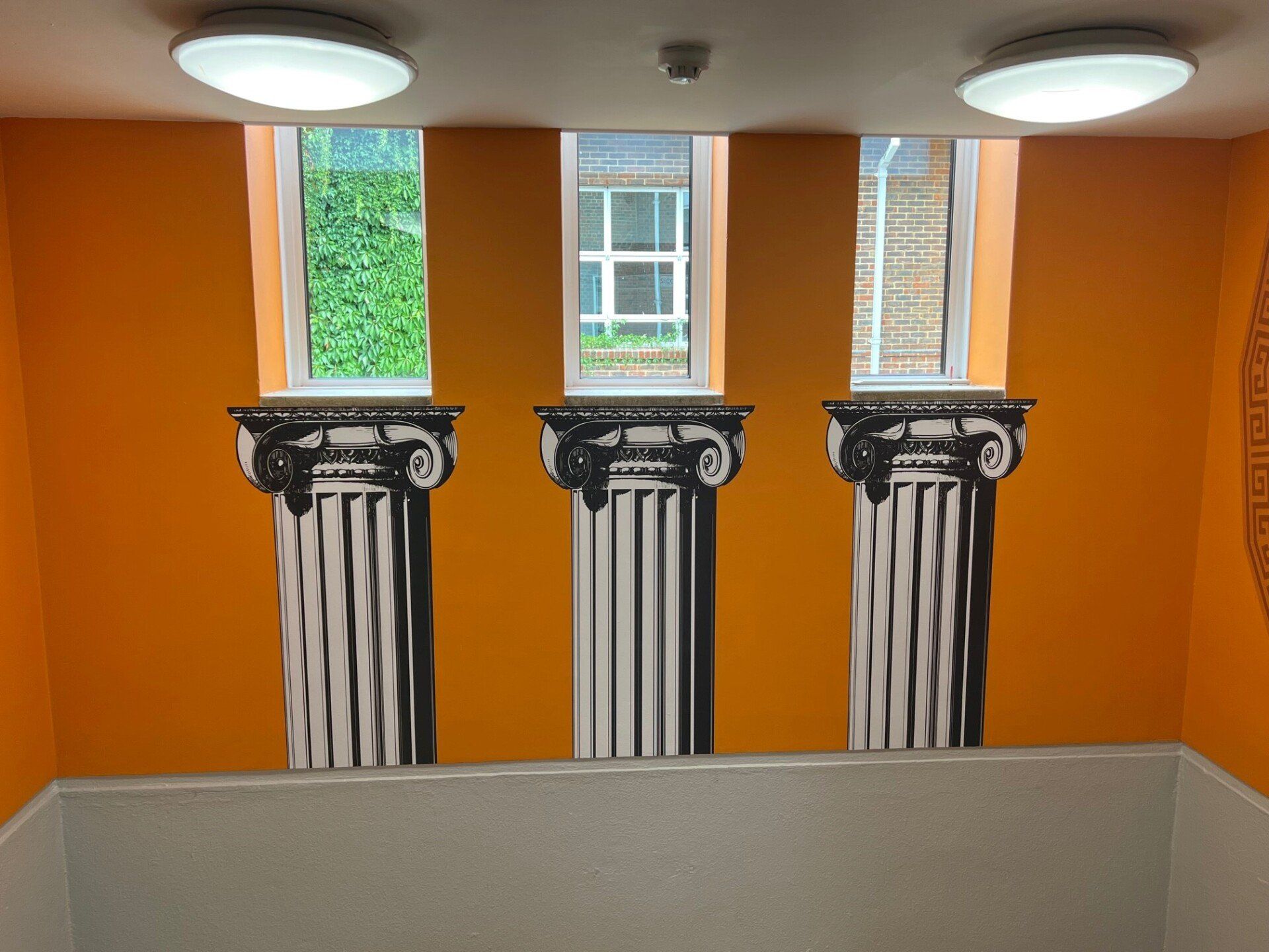 Three columns are painted on an orange wall next to a window.