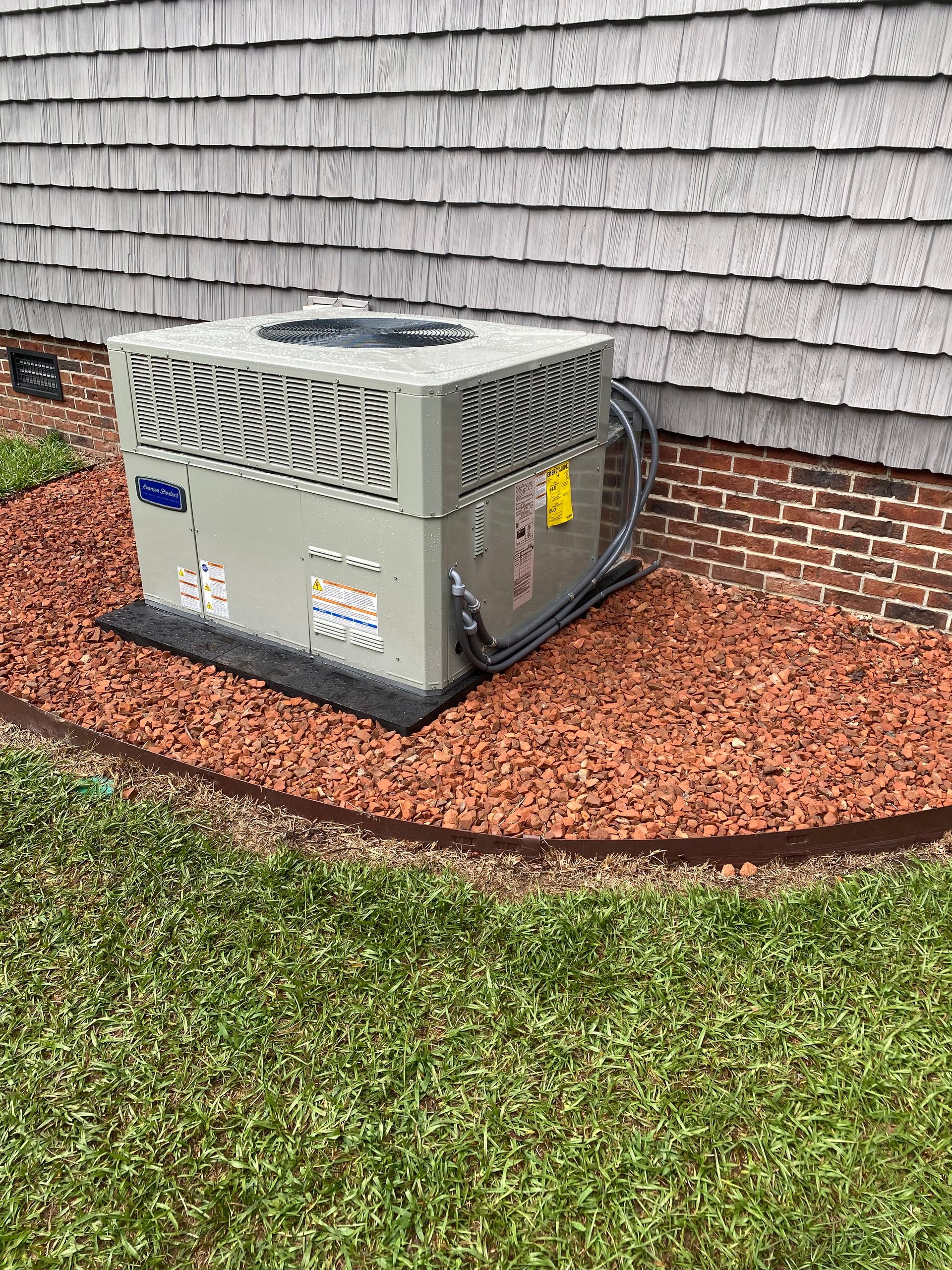 an air conditioner is sitting on top of a pile of mulch next to a house .