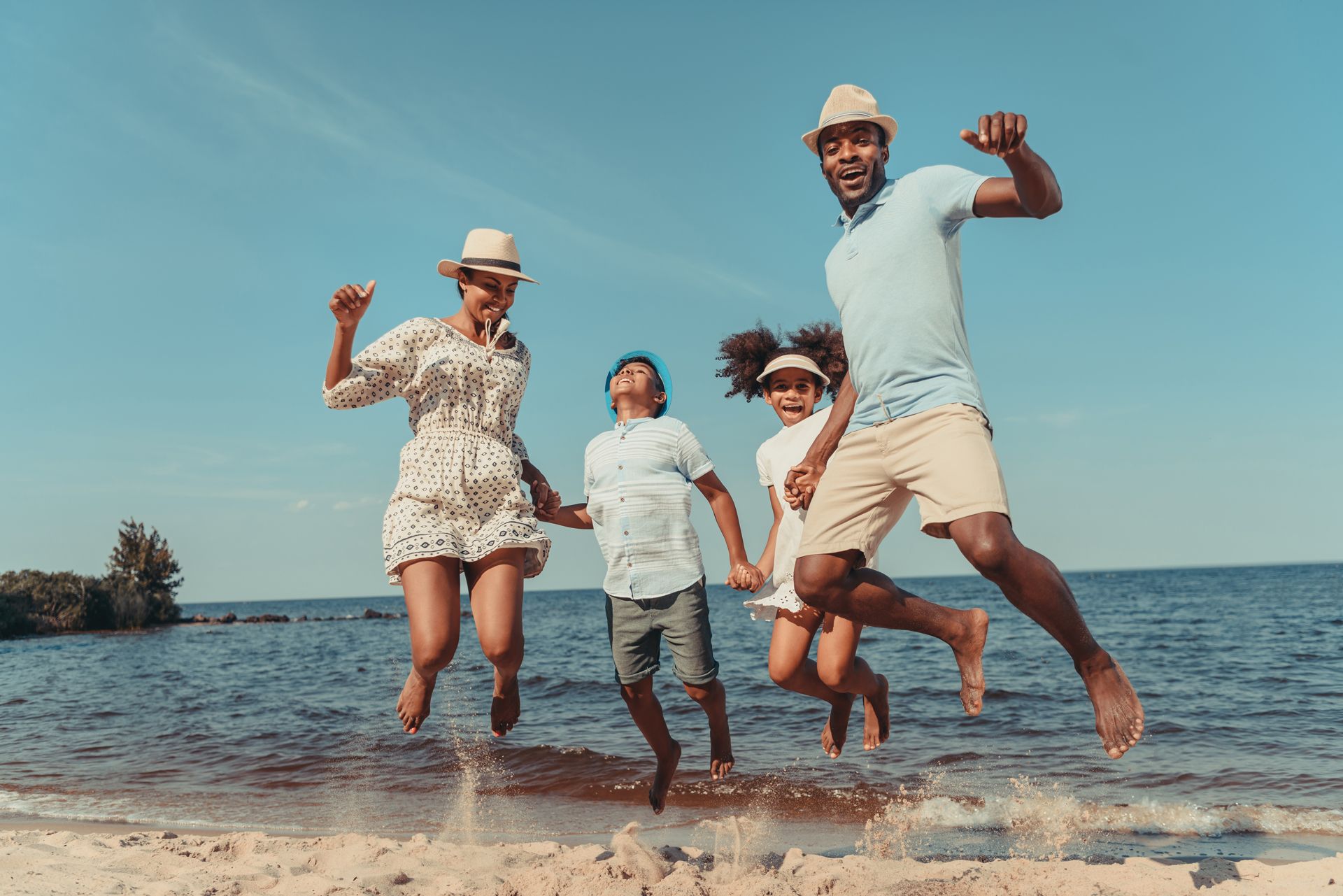 Family, jumping for joy on a beach. The parents and two kids are wearing summer clothes, on a sunny day