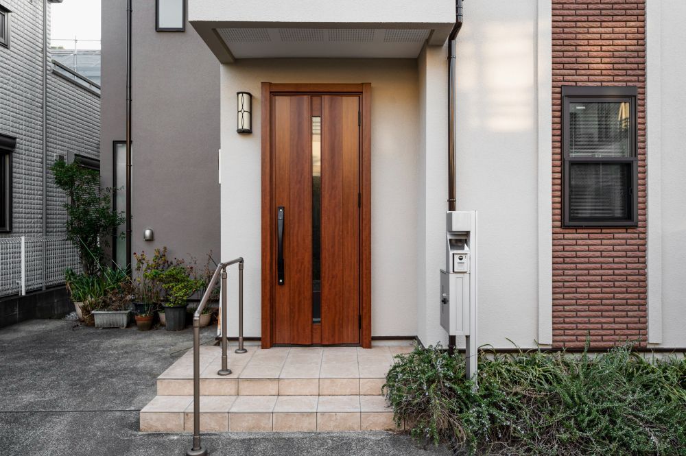 Wooden front door with glass insert, recessed entry, brick and gray exterior.