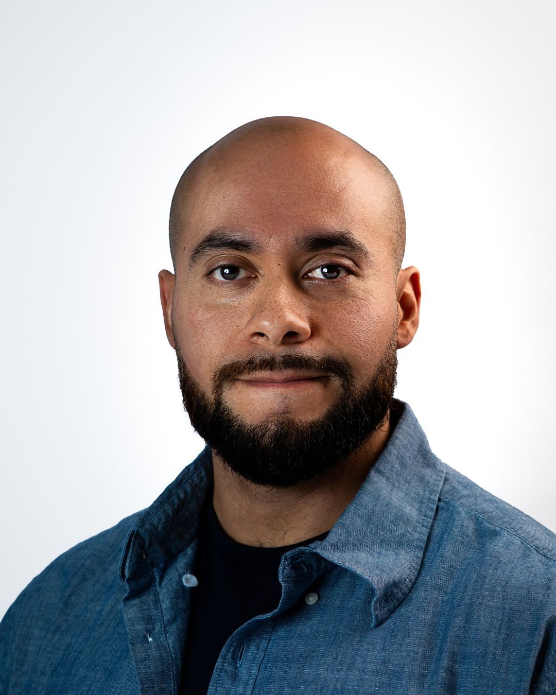 Portrait of a bald man with a beard in a teal shirt against a dark background