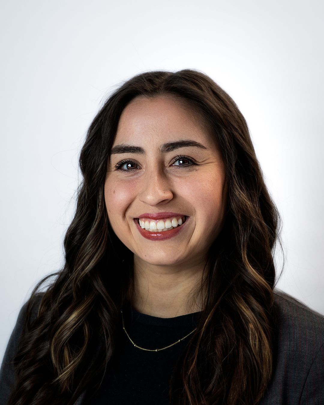 Portrait of a smiling person with long brown hair wearing a black shirt against a gray background