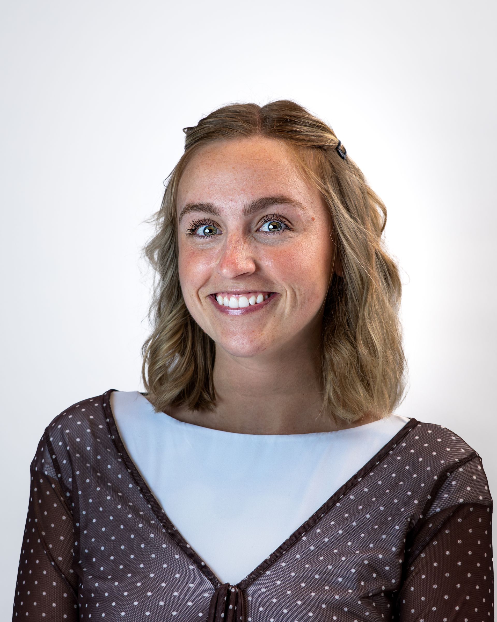 Smiling person in a cream knit sweater against a gray studio backdrop