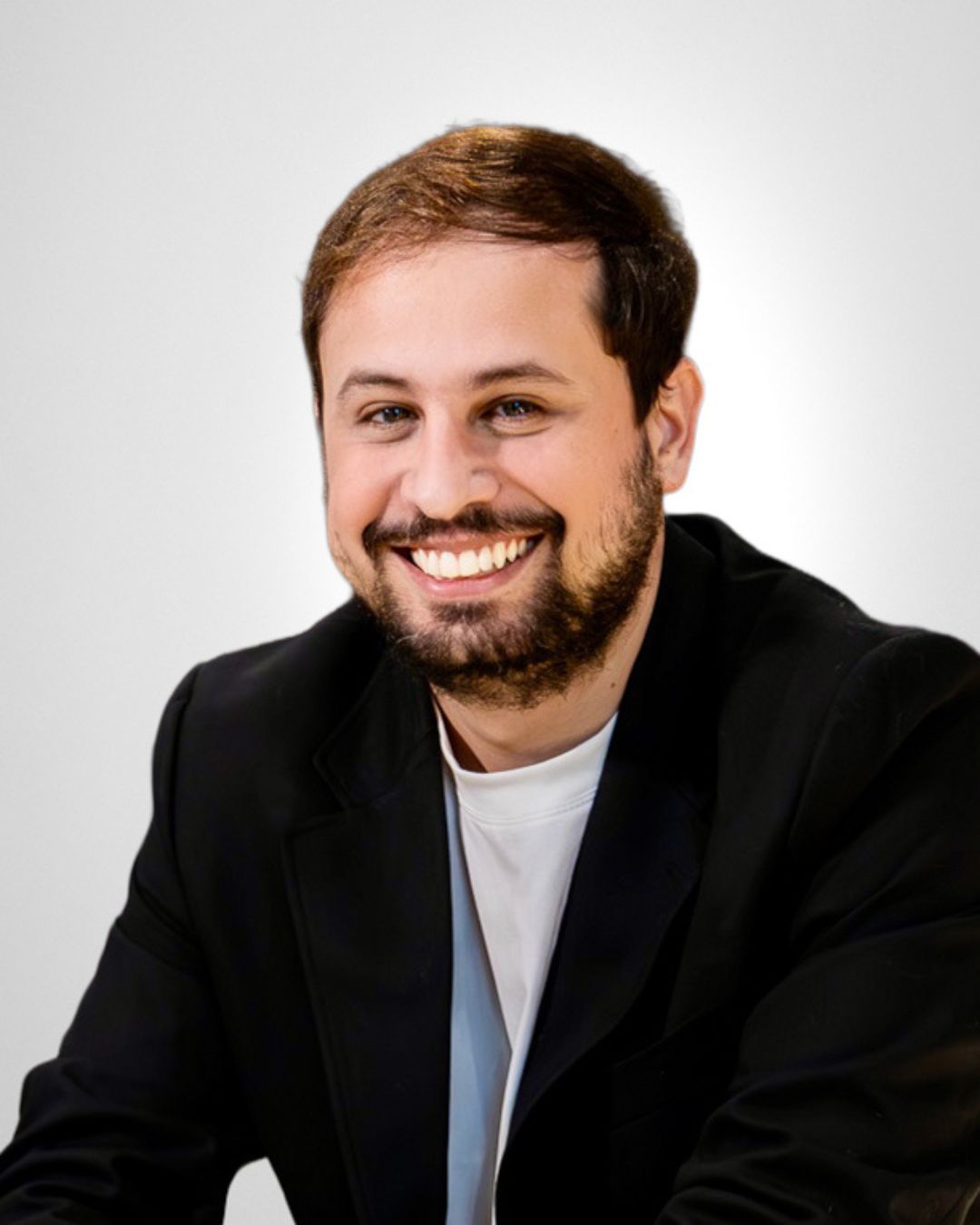 Smiling man in a coral sweater against a gray studio background
