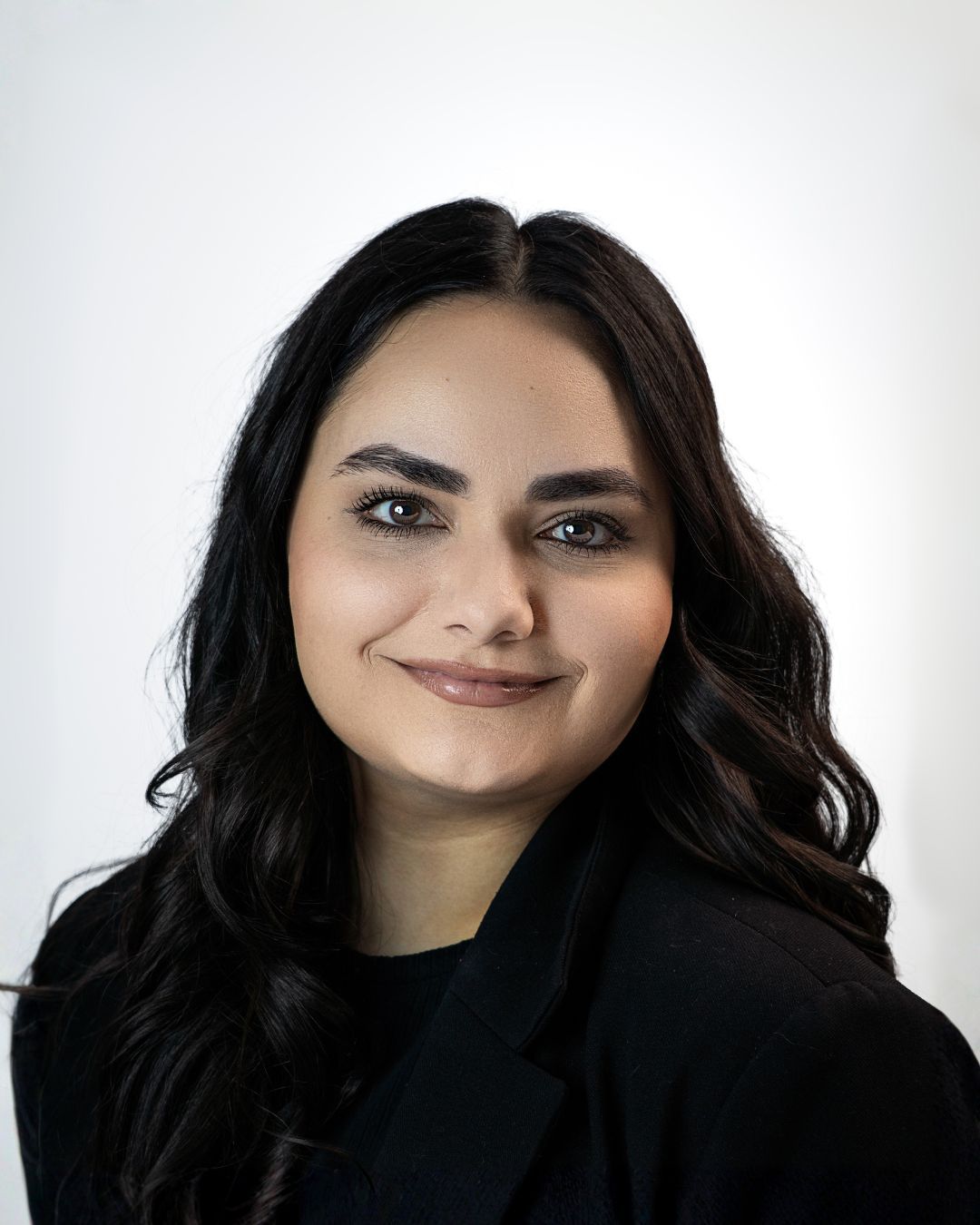 Portrait of a smiling woman with long dark wavy hair against a gray studio backdrop