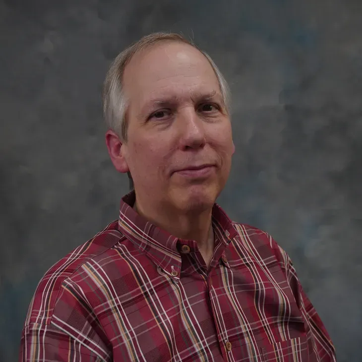 Portrait of a man in a red plaid shirt against a gray studio backdrop