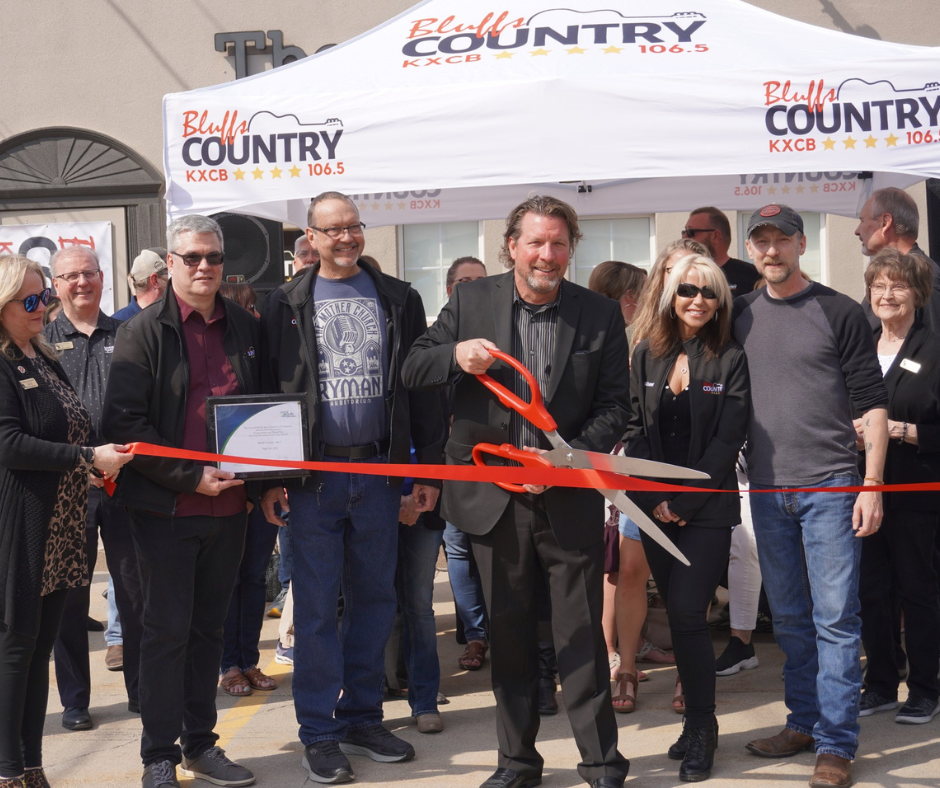 A group of people standing under a branded canopy during a ribbon-cutting ceremony.