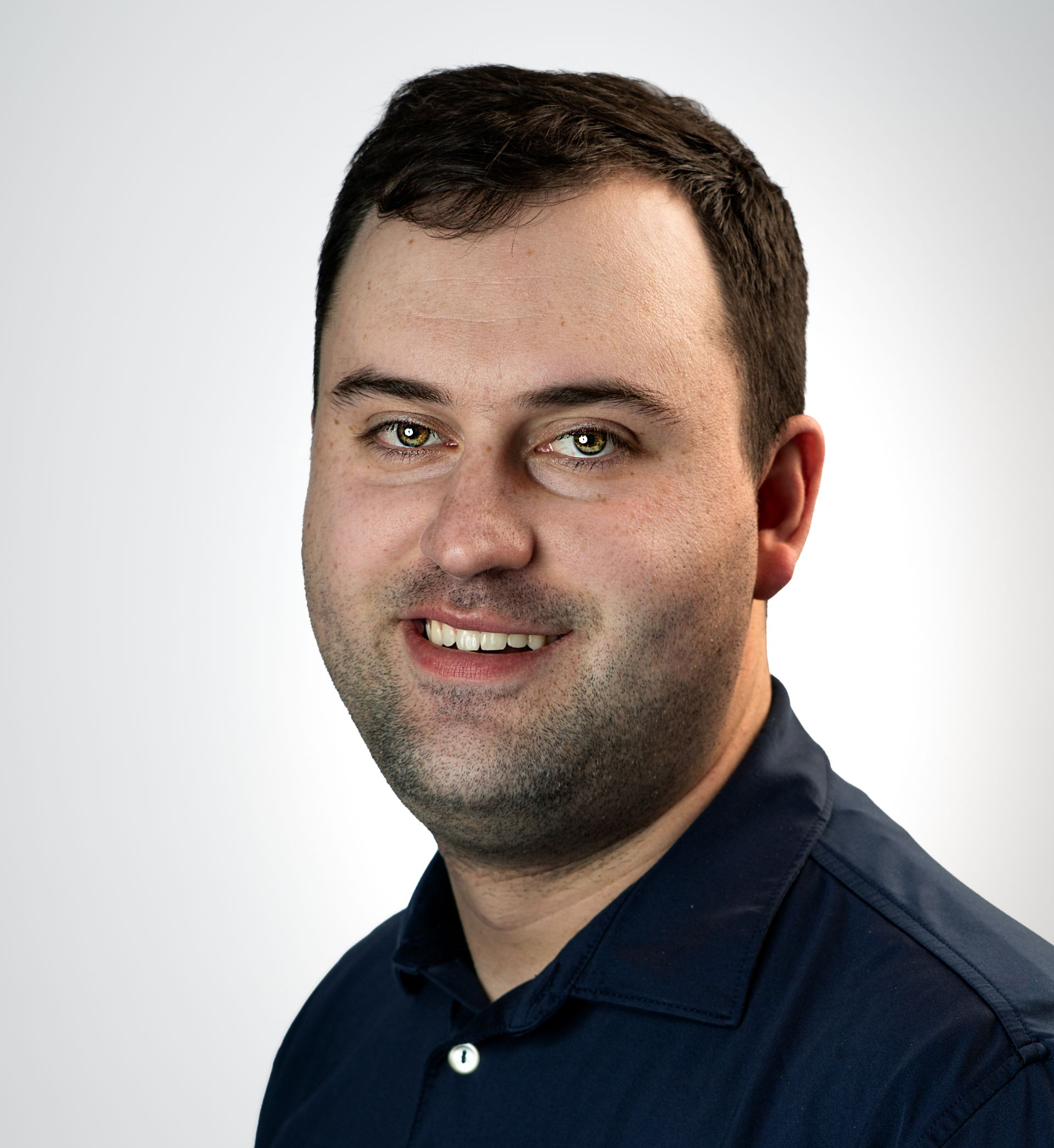 Portrait of a smiling person in a purple striped polo shirt against a gray studio backdrop