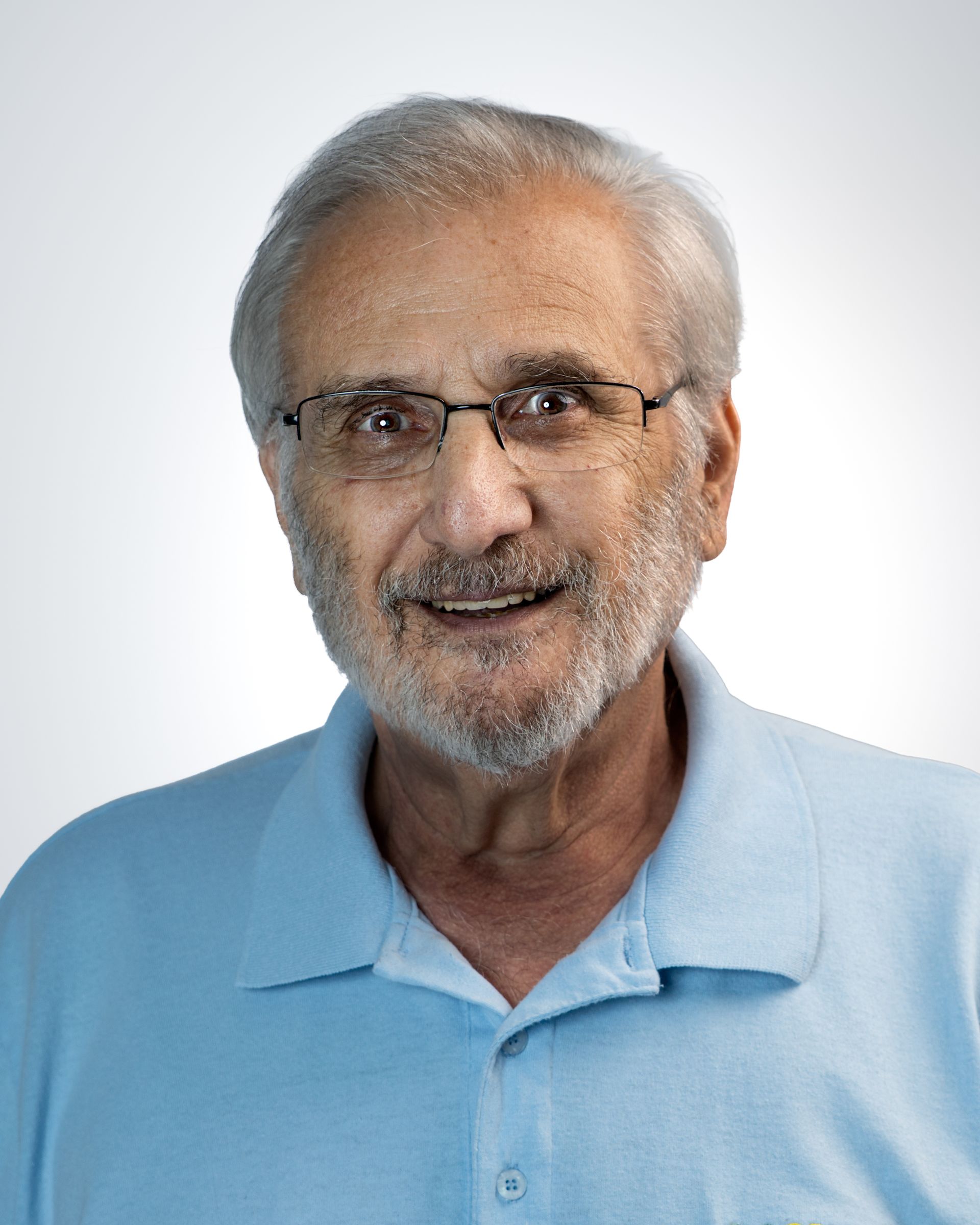 Smiling man with gray hair, glasses, and a white polo shirt against a gray studio backdrop