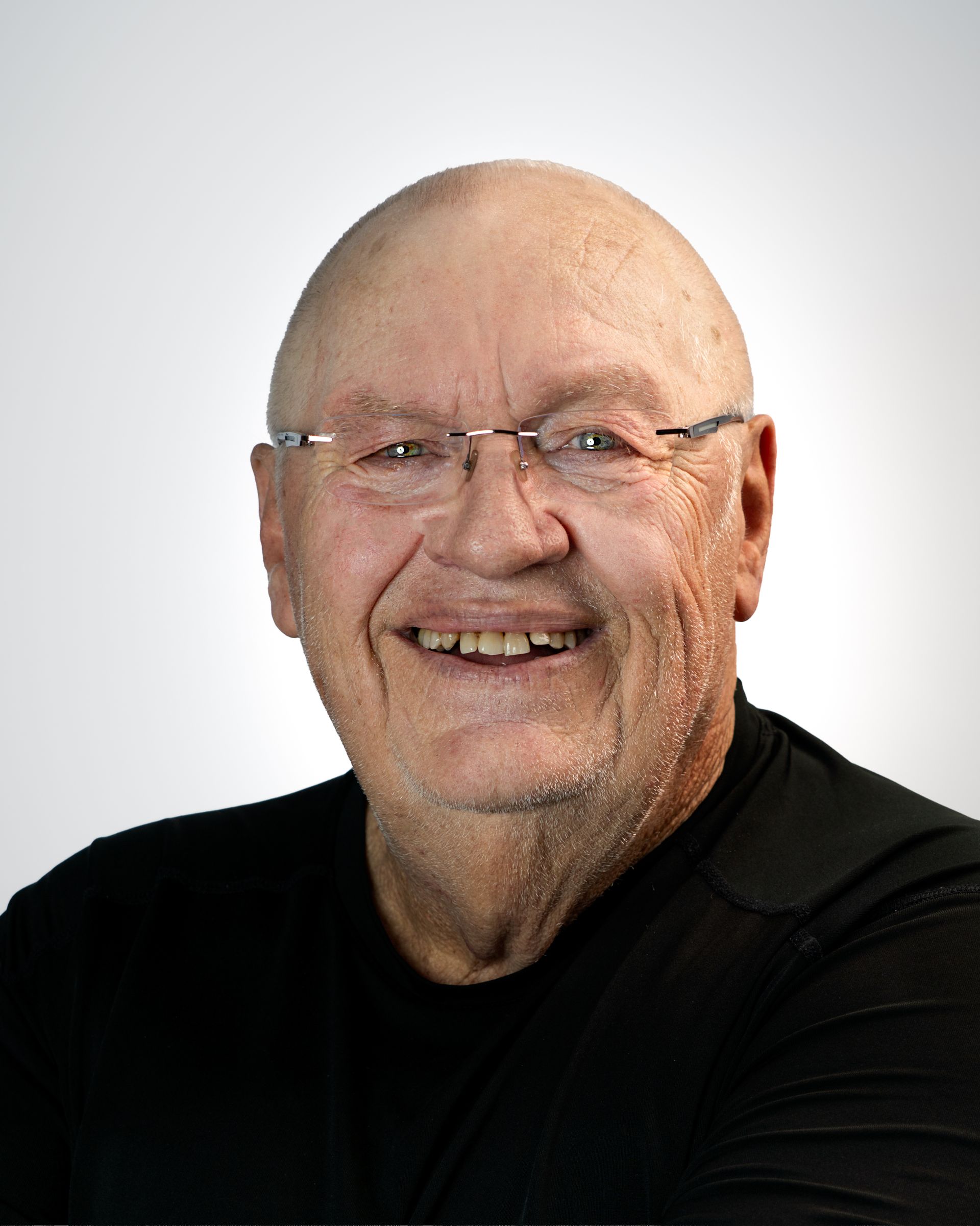 Smiling bald man in a purple checkered shirt against a gray studio backdrop