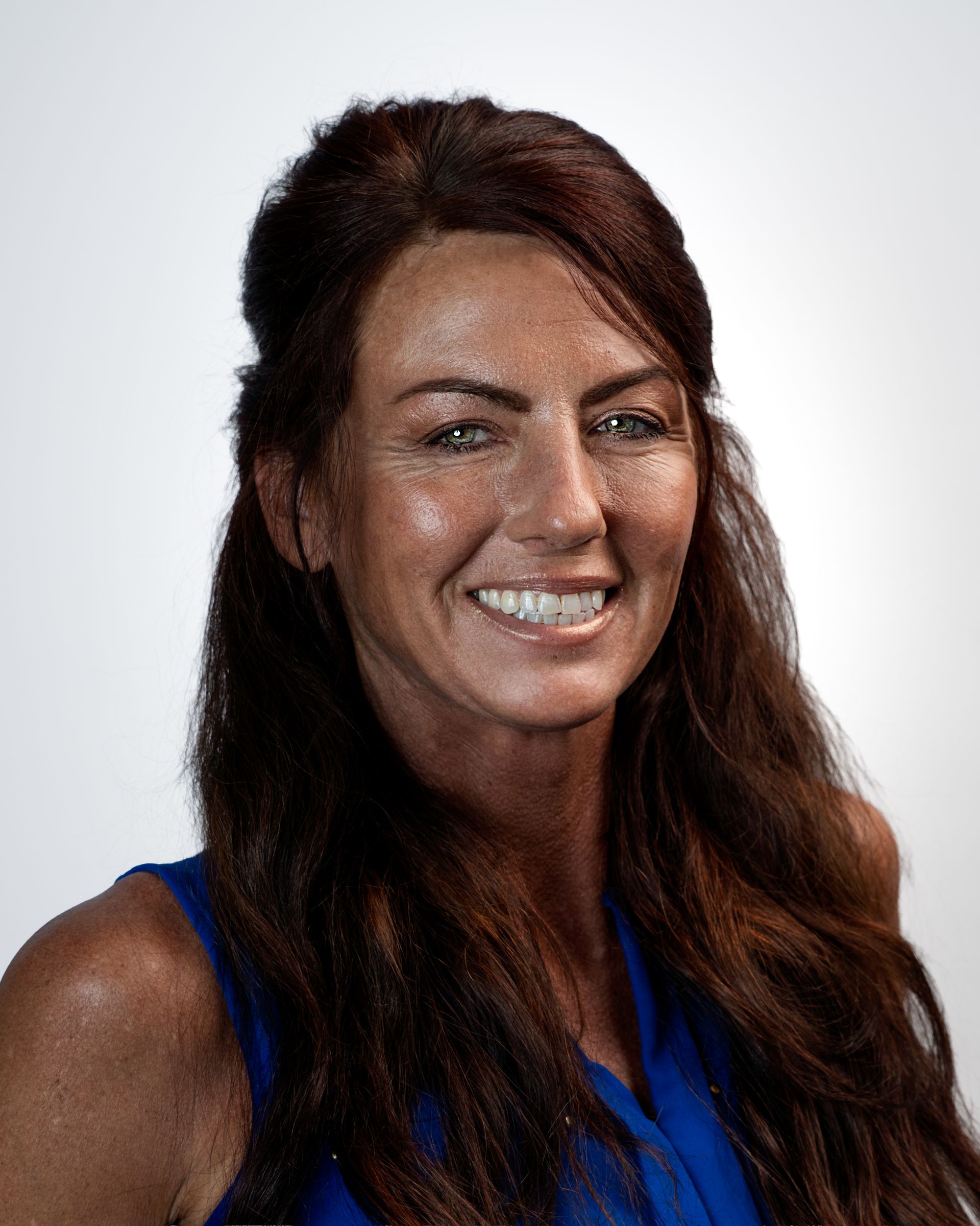 Portrait of a smiling woman with long brown hair against a gray studio backdrop