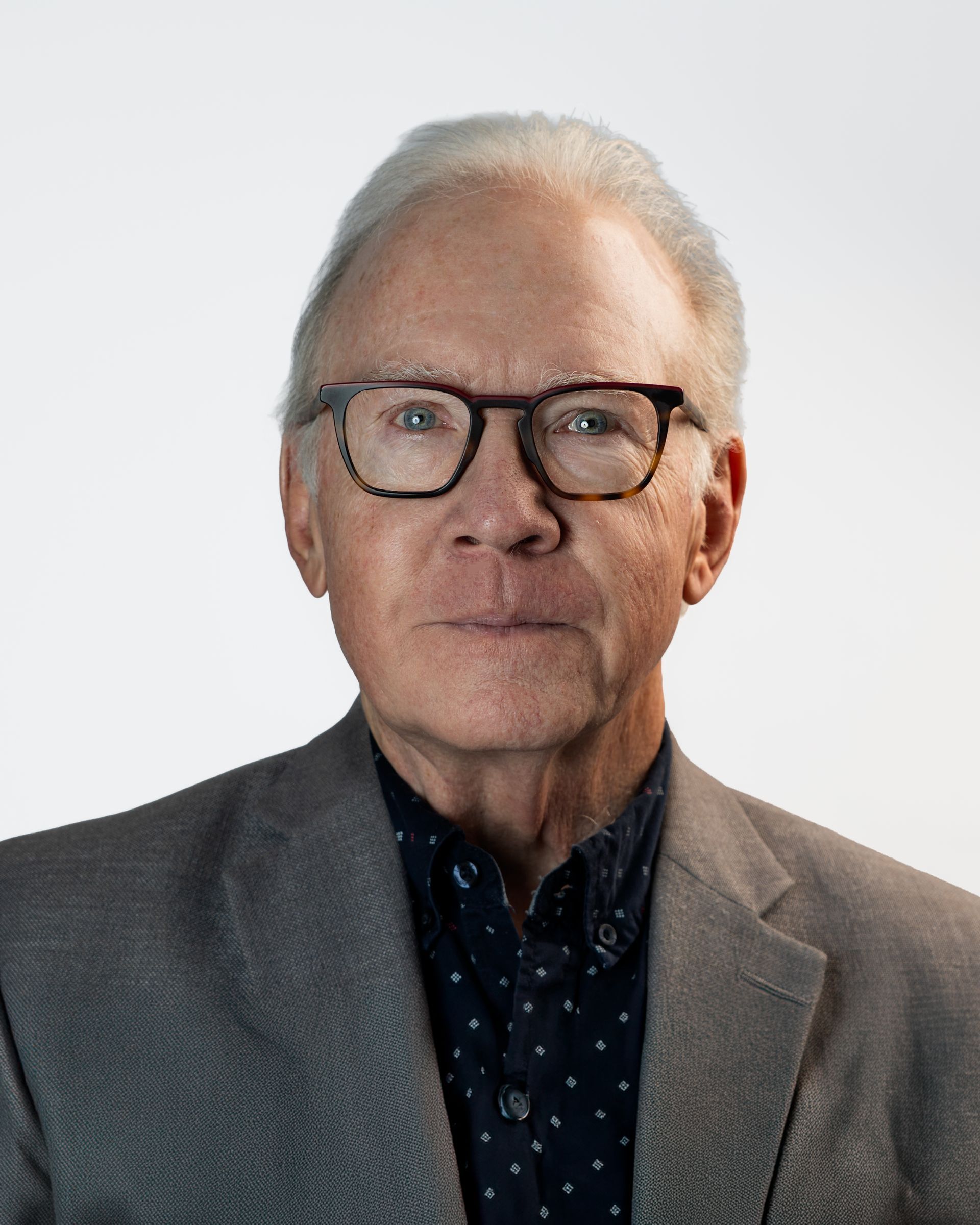 Portrait of a smiling man in glasses wearing a dark blazer against a gray studio backdrop