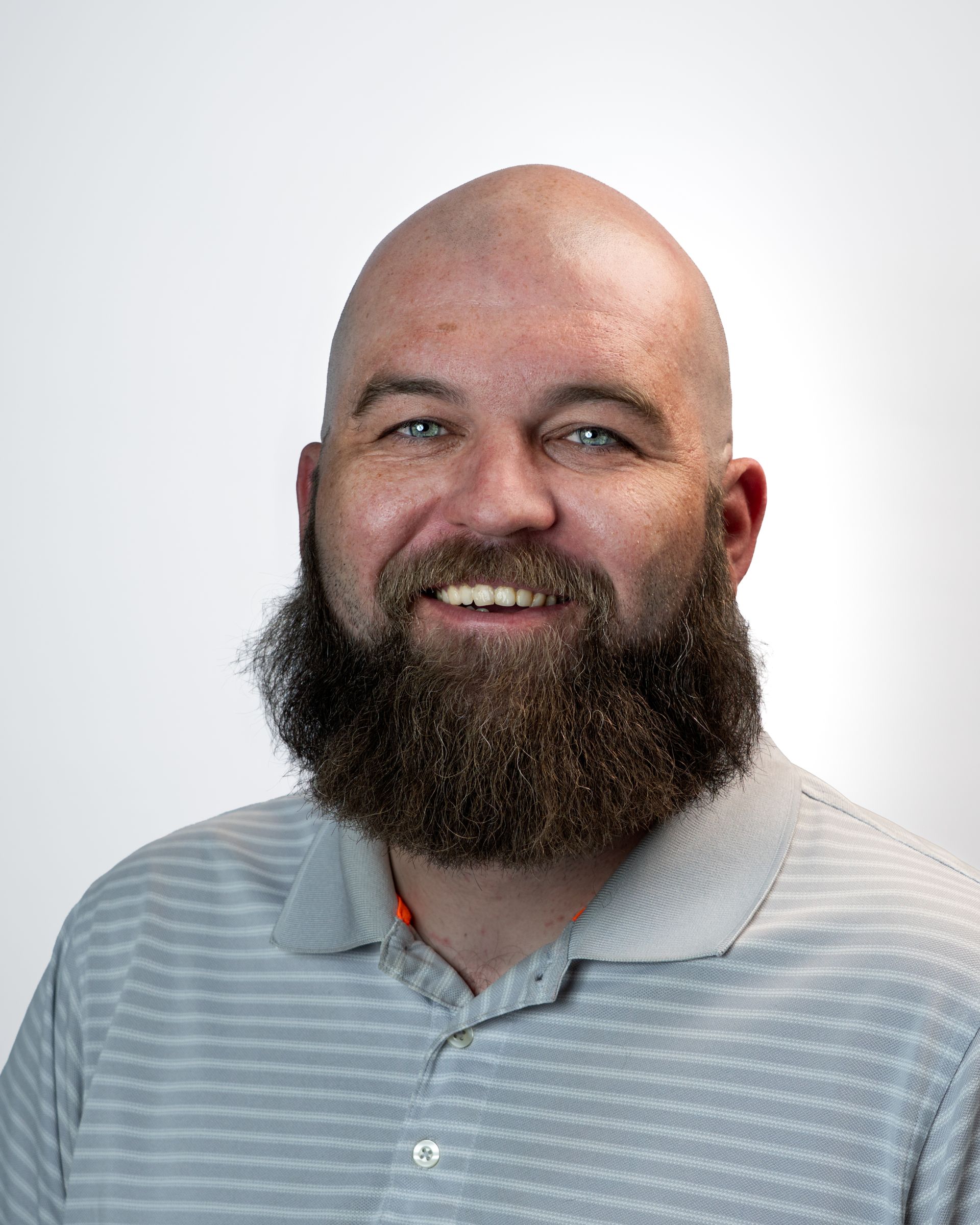 Smiling bald man with a long beard wearing a dark gray jacket against a gray backdrop