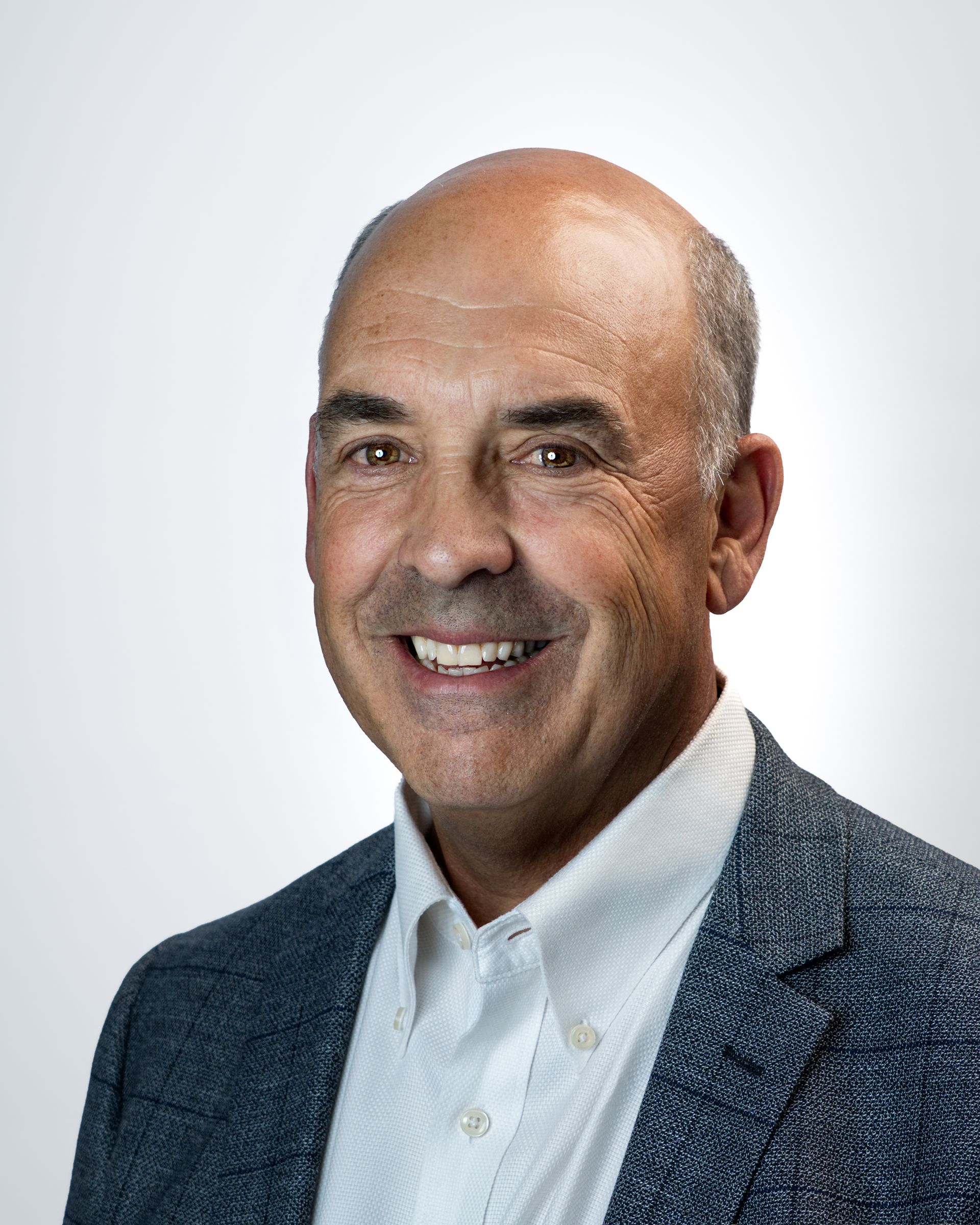 Smiling bald man in a light blue blazer against a dark studio background