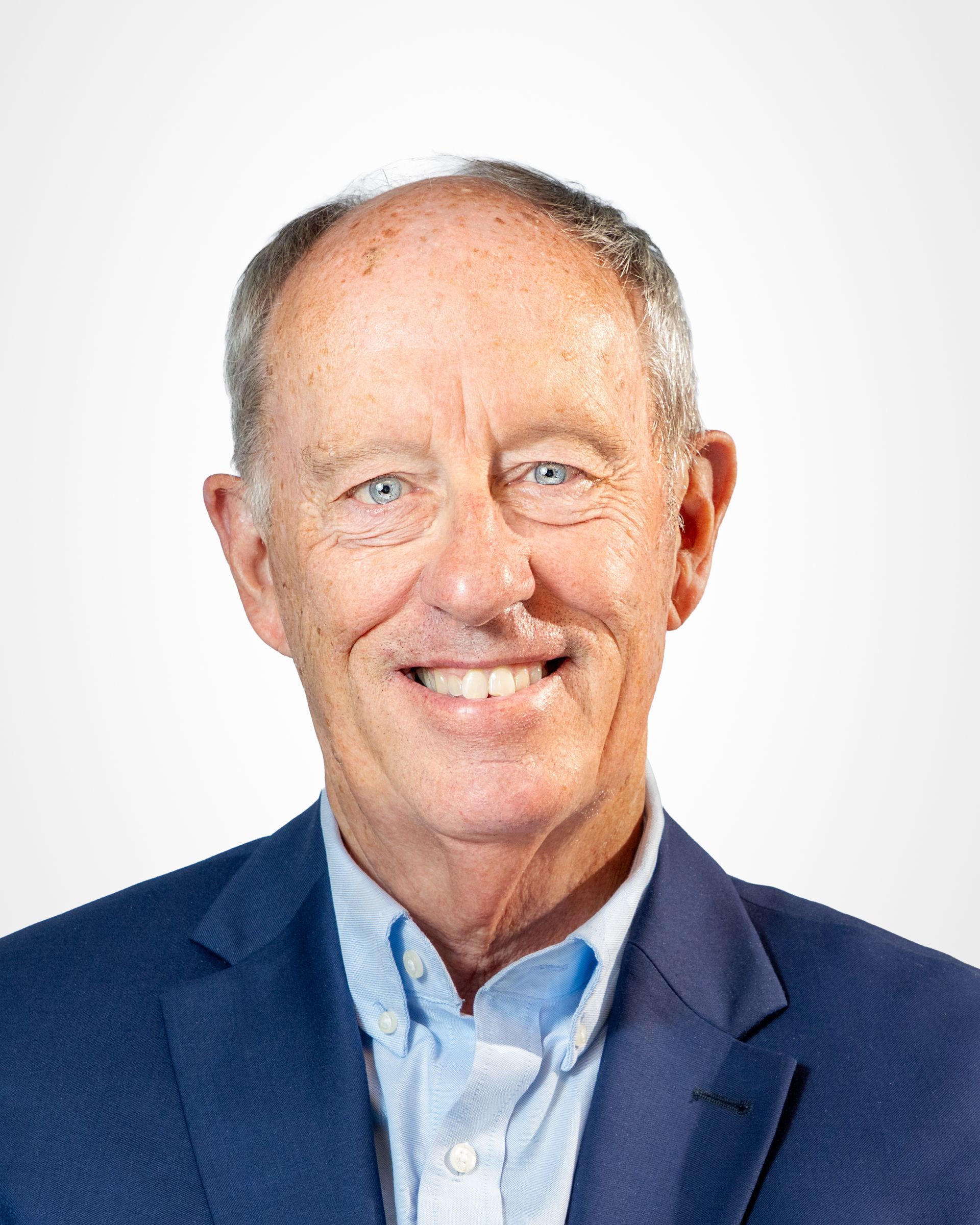 Portrait of a smiling man in a navy blazer and blue shirt against a gray studio background
