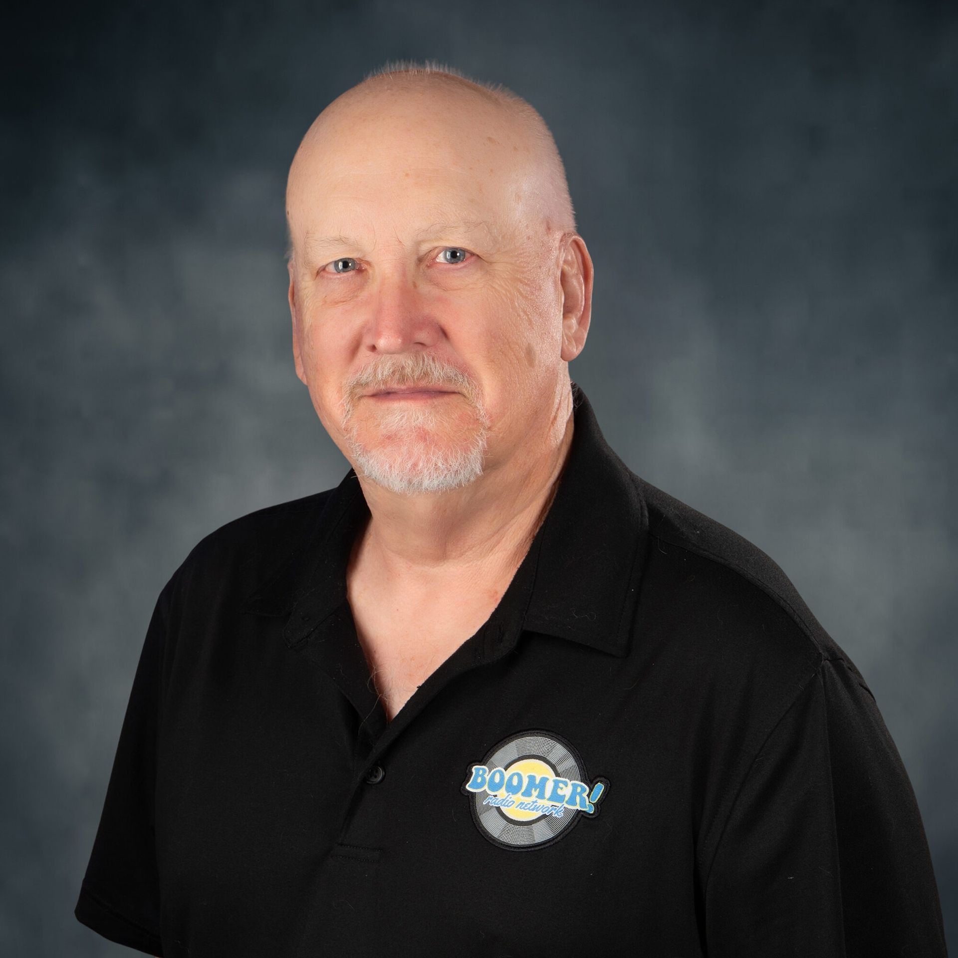 Portrait of a man in a black polo shirt with a logo, against a gray studio backdrop