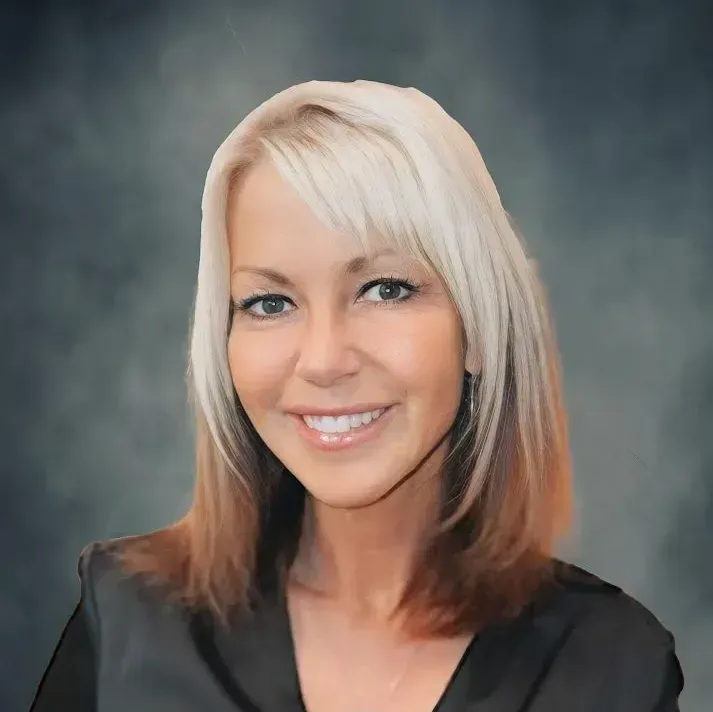 Portrait of a smiling woman with blonde hair against a gray studio backdrop