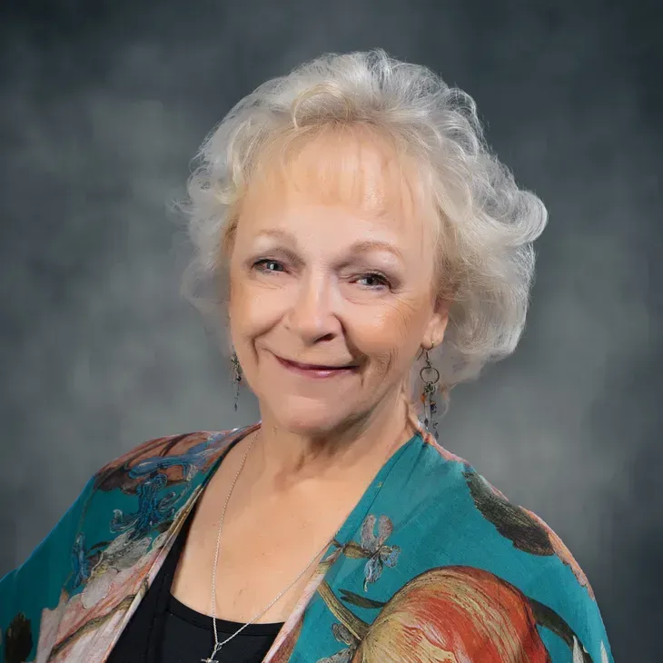 Portrait of a smiling woman in a turquoise shawl against a gray studio backdrop