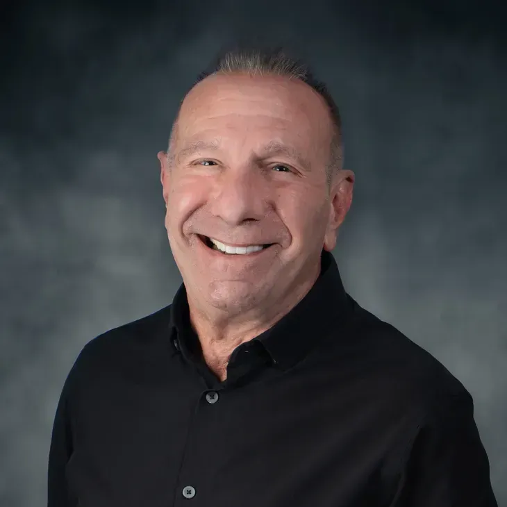 Smiling man in a black shirt against a gray studio backdrop