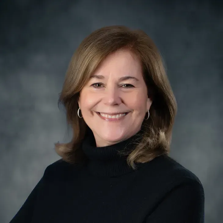 Smiling woman in a black turtleneck against a gray studio backdrop