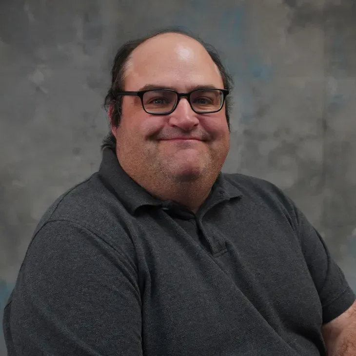 Smiling man in glasses and a dark polo shirt against a gray background