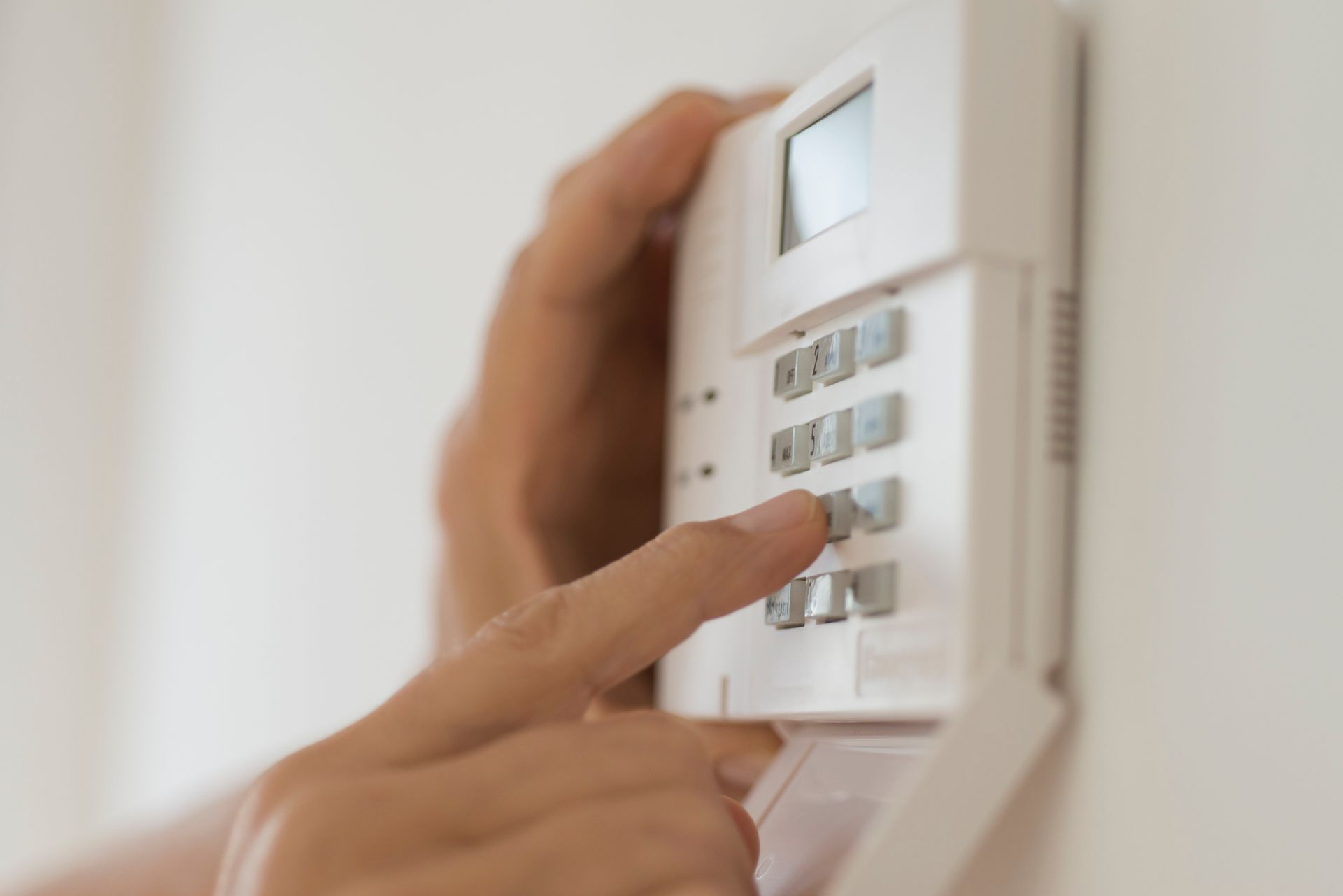 Persona che digita un codice su una tastiera bianca di sicurezza domestica montata su una parete bianca.