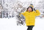 Person in a bright yellow jacket and winter hat standing in a snowy park, smiling