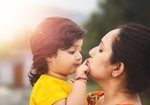Woman kissing toddler's cheek while holding them close outdoors, both in soft focus