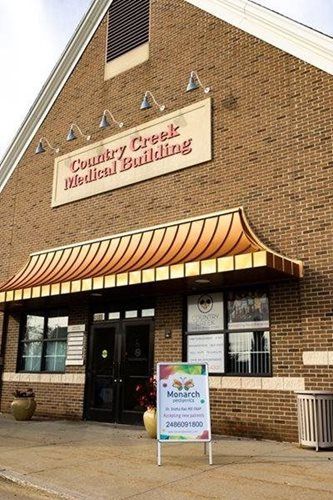 A brick Country Creek Medical Building with a tan awning and a colorful sandwich board sign on the sidewalk.