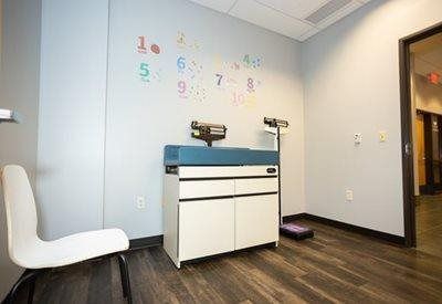 A medical exam room features a white chair, a cabinet with a scale on top, and wall decals of numbers one through ten.