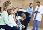 Family sitting in a clinic waiting room, with a doctor and nurse in the background