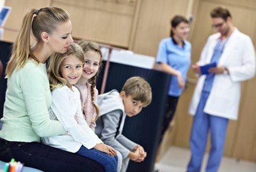 Family waiting in a clinic, sitting on a bench while doctors talk in the background