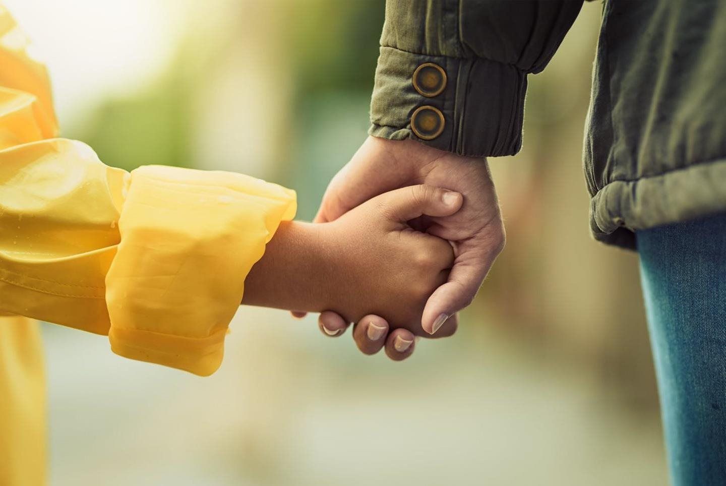 A person wearing a yellow sleeve holds the hand of another person wearing a green jacket in an outdoor setting.