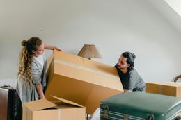 A man and a woman are holding a large cardboard box in a living room.