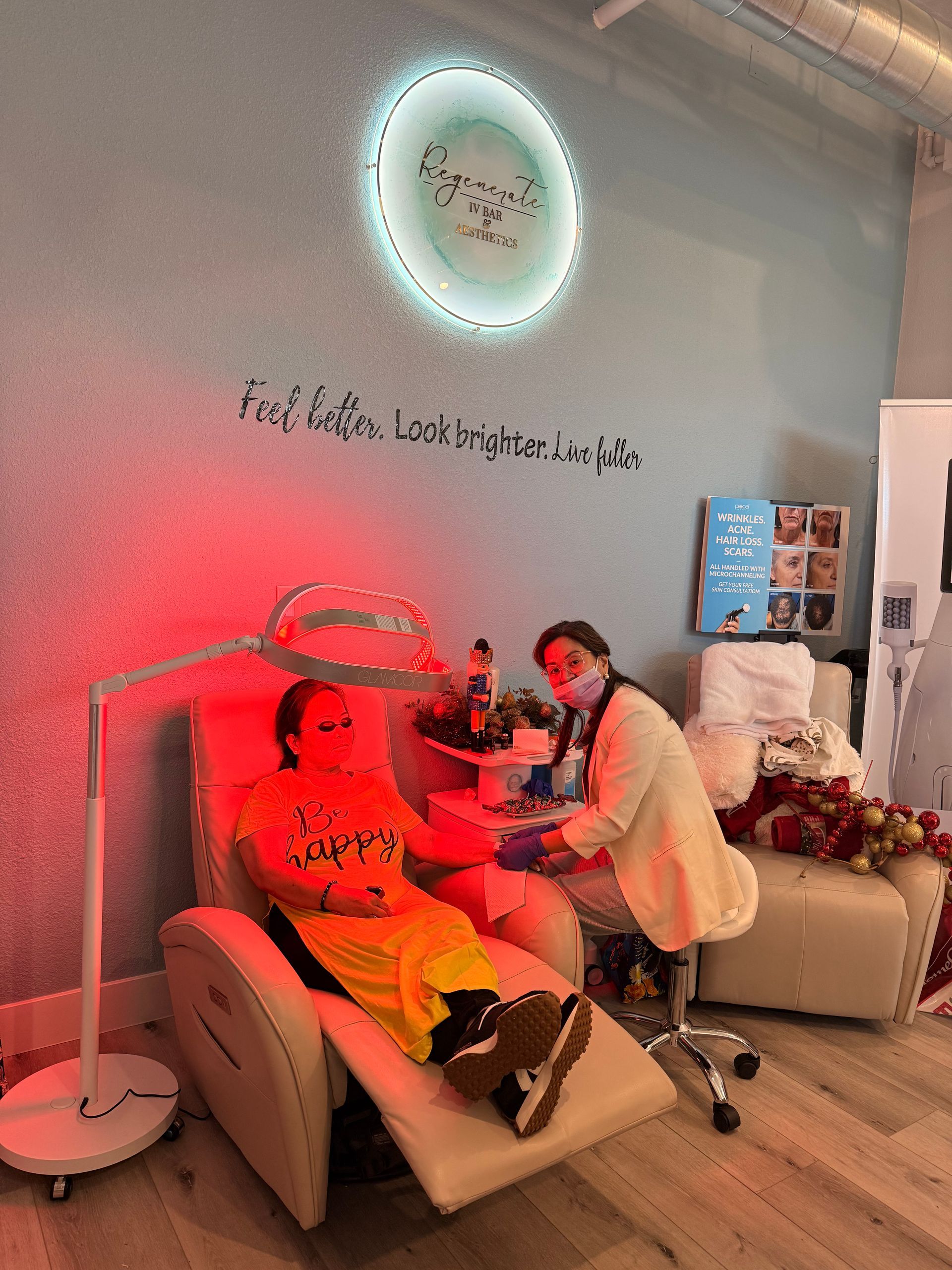 A person receives IV therapy in a reclining chair while a professional adjusts the drip under a red light in a clinic.