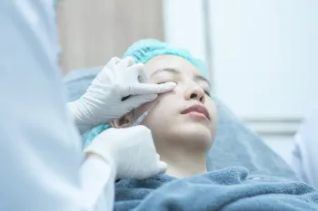 Person receiving a facial peel treatment. A gloved hand applies a liquid from a brush to the forehead.