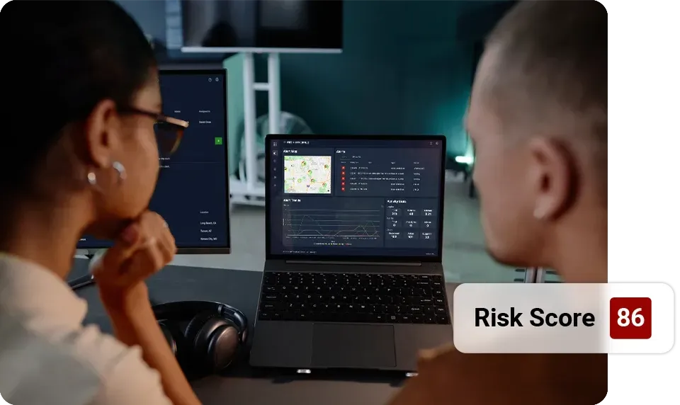 Two people reviewing a laptop with a risk score of 86 displayed, likely analyzing data.