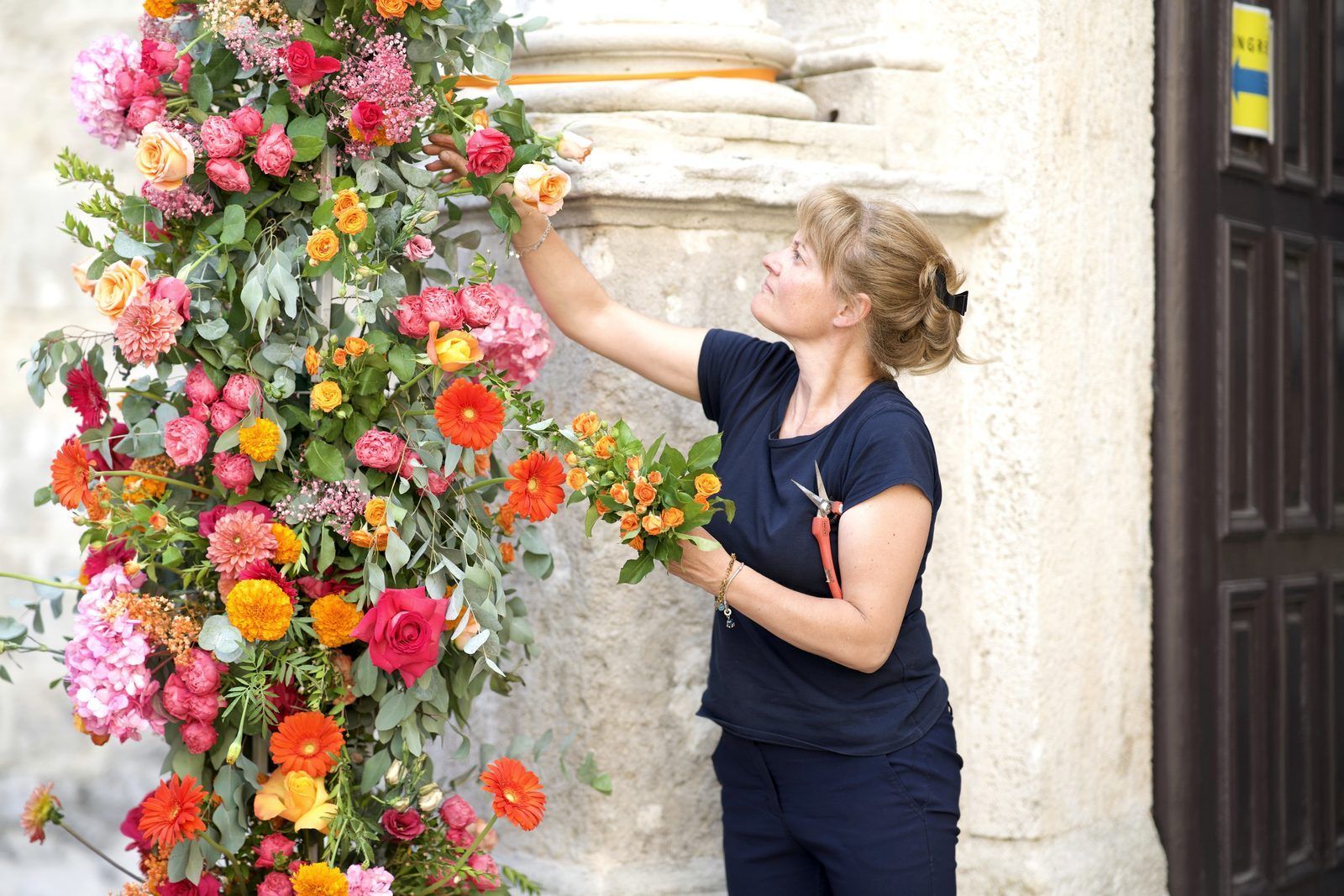 Una fiorista compone una colonna di fiori sul portale in pietra di una chiesa