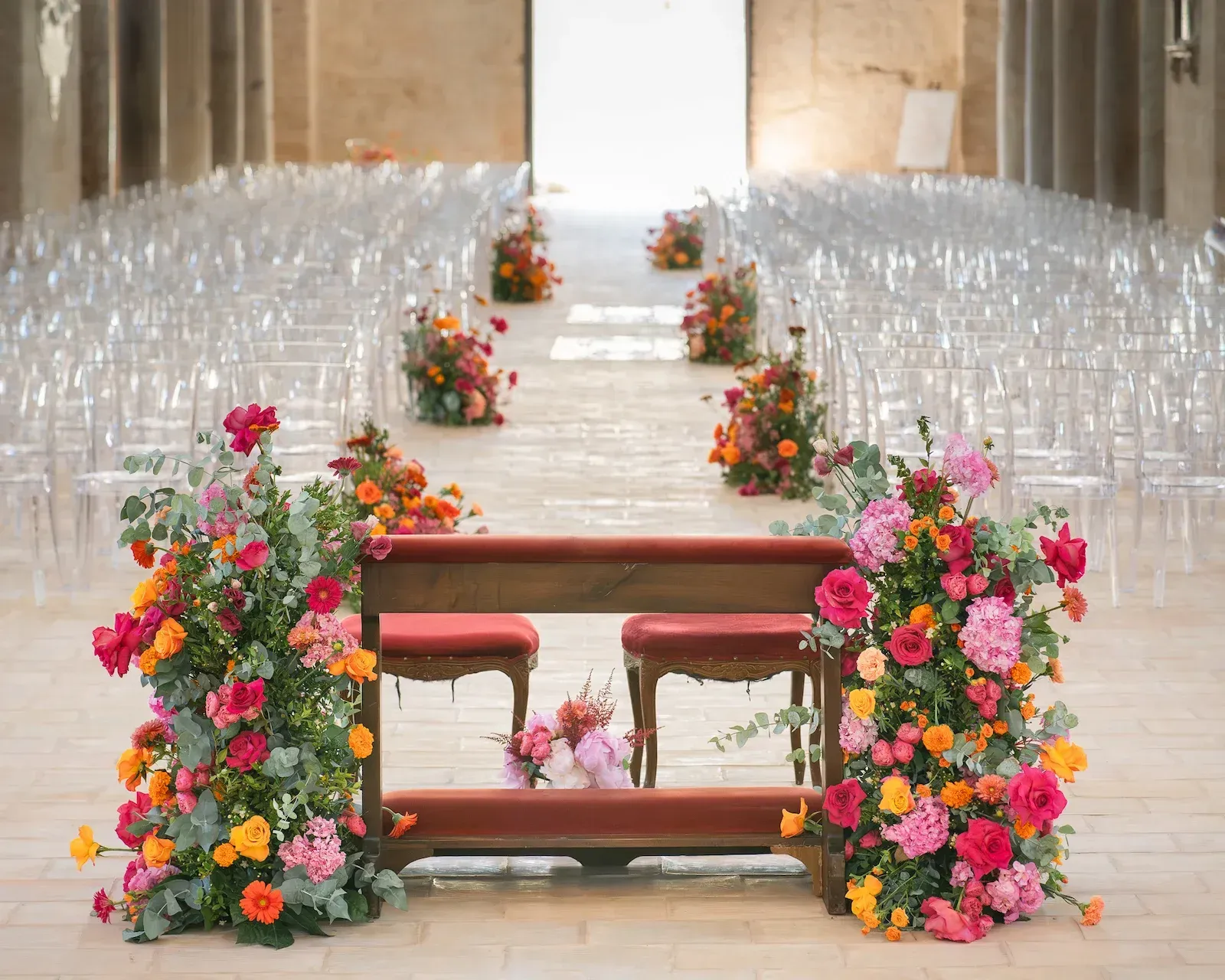 Inginocchiatoio per gli sposi fra due grandi composizioni di fiori rosa e arancioni, con la navata allestita alle spalle