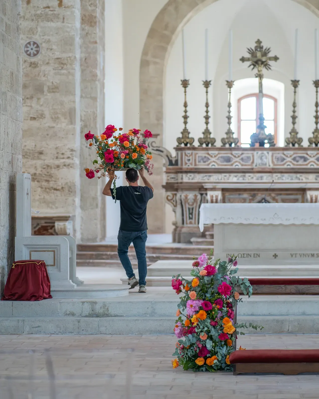 L’allestimento in corso: un collaboratore porta una composizione verso l’altare, con i primi fiori già lungo la navata