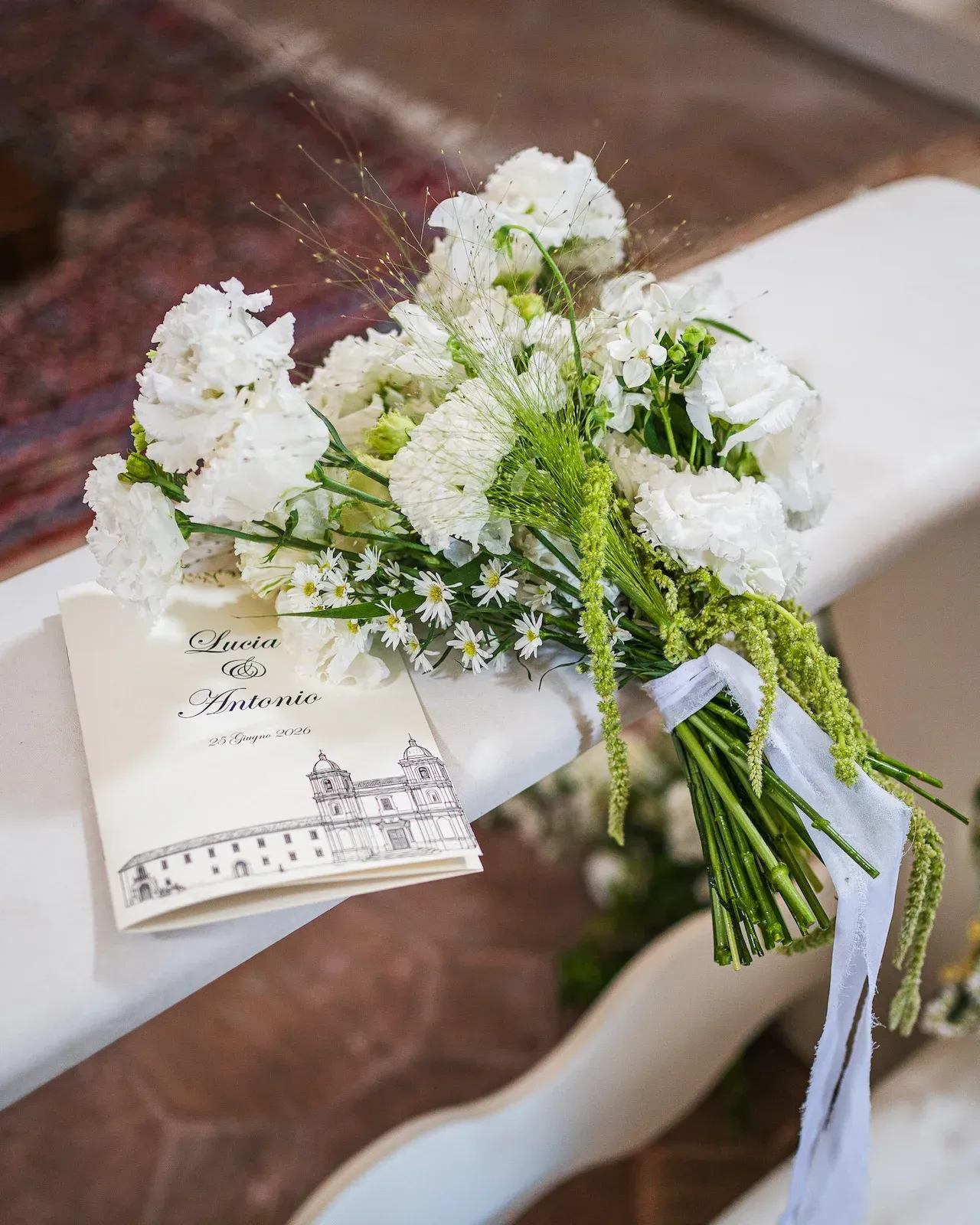 Mazzo di fiori bianchi con nastro appoggiato sul libretto della cerimonia